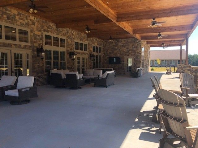 A spacious outdoor patio area with comfortable seating, a stone wall backdrop, and wooden ceiling featuring ceiling fans.