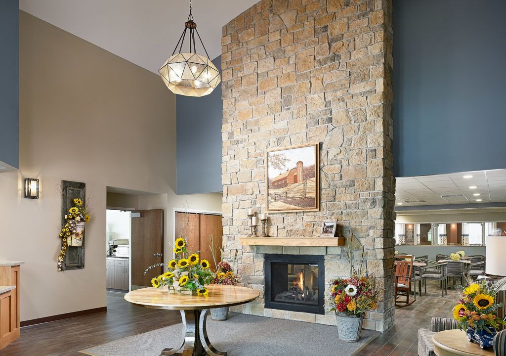 A cozy living room featuring a tall stone fireplace, a chandelier, and a central table with sunflowers.