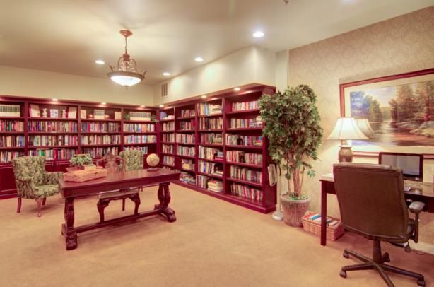 A cozy library with bookshelves, a wooden table, and a desk with a lamp.