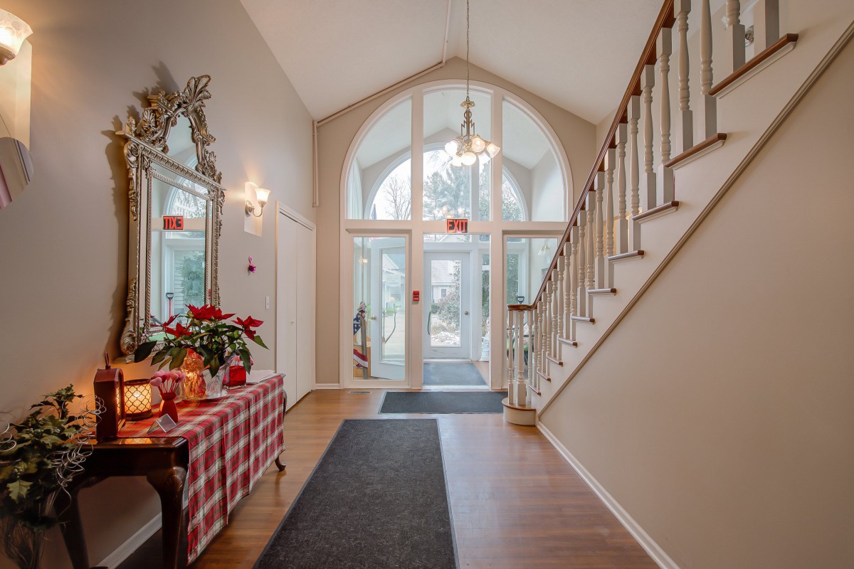 A welcoming foyer with a staircase, wood flooring, and a decorated table near large windows.