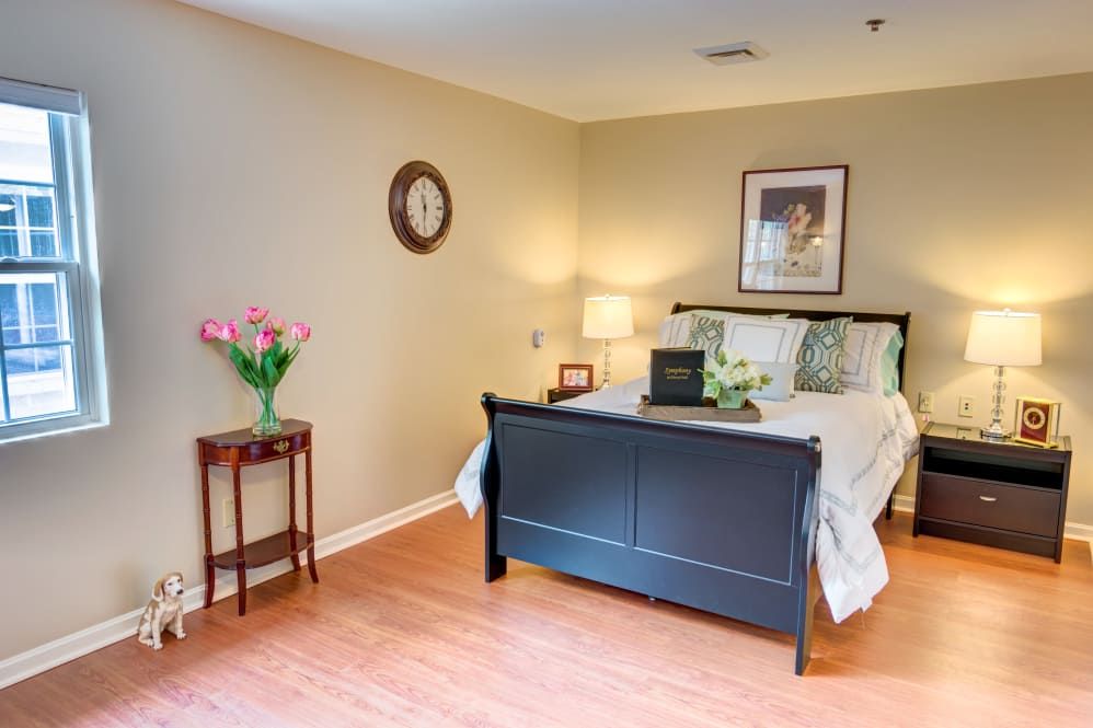 A cozy bedroom with a dark wooden bed, side table with pink flowers, and a decorative wall clock.