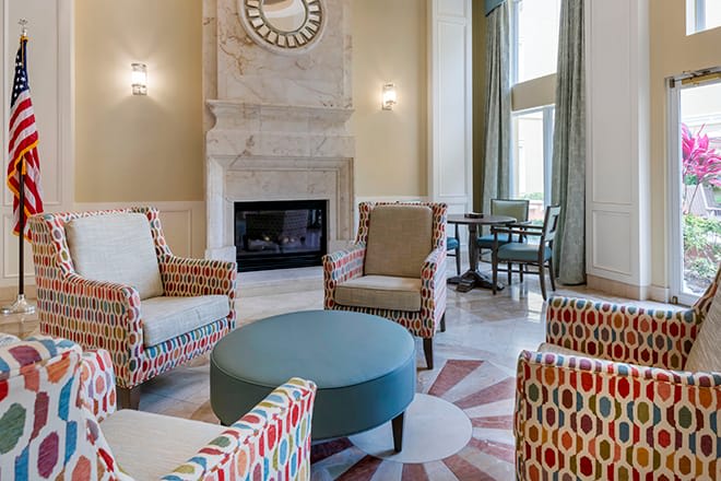 A stylish living room featuring patterned armchairs, a central ottoman, and a classic fireplace.