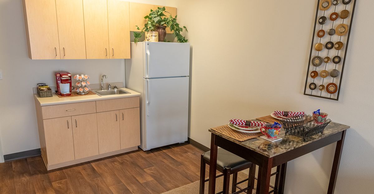 A compact kitchen and dining area featuring a refrigerator, sink, and a table with place settings.