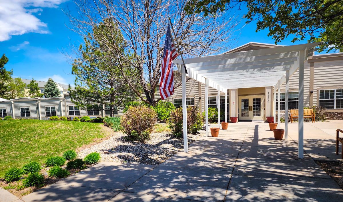 A building entrance with an American flag, surrounded by trees and landscaping on a sunny day.