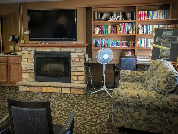 A cozy living room featuring a stone fireplace, a large television, and a bookshelf filled with books.