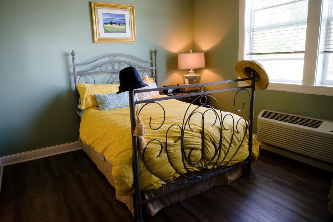 A cozy bedroom with yellow bedding and hats on the bedpost.