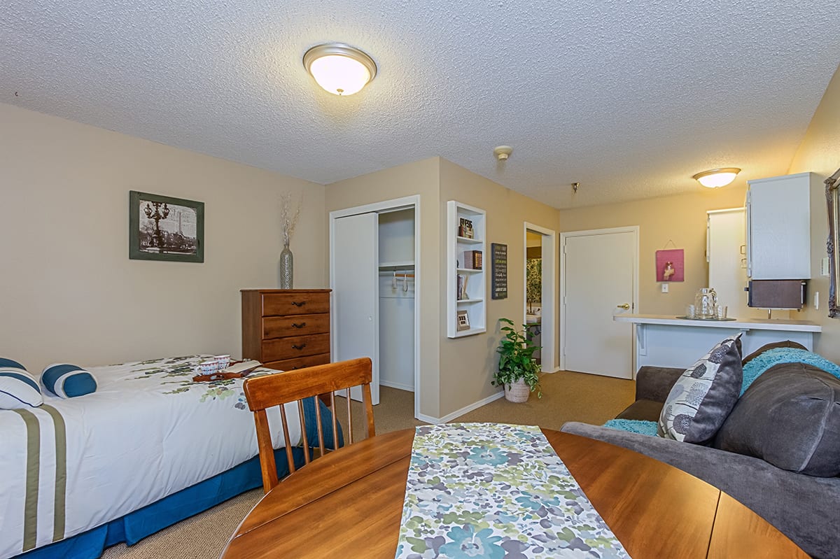 A cozy bedroom with a small dining area, featuring a bed, dresser, and a table with chairs.