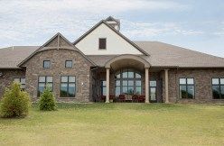 A stone exterior residential house with a large lawn and columns.