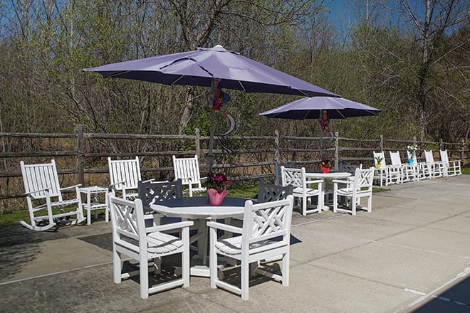 An outdoor patio area with white tables and chairs, shaded by purple umbrellas.