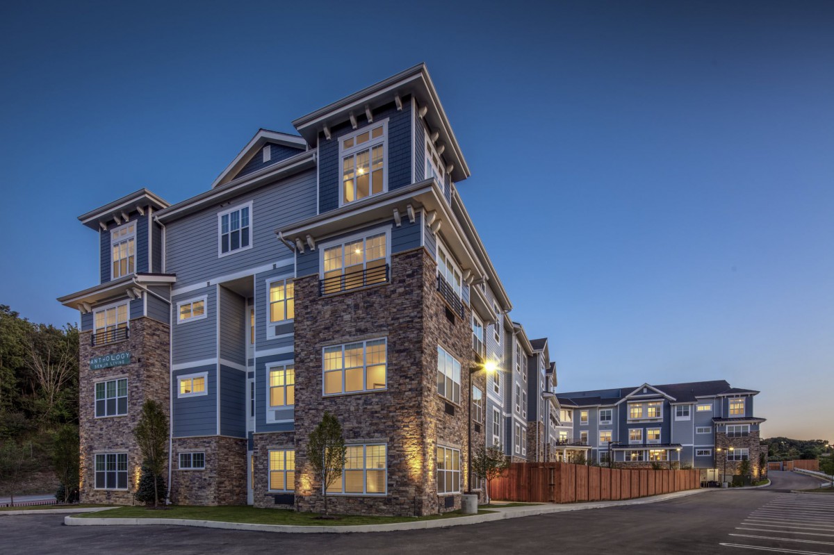 A modern apartment building with a stone facade, illuminated at dusk.