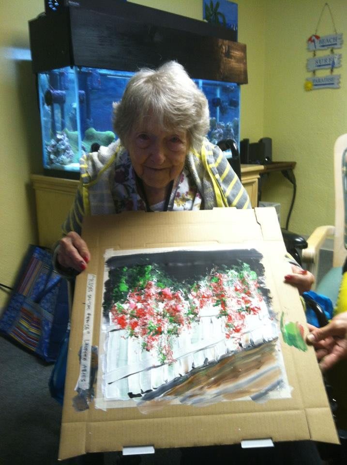 An elderly woman proudly displaying her painting next to an aquarium.