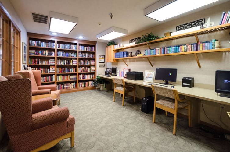 A cozy library reading area with bookshelves, computers, and comfortable chairs.