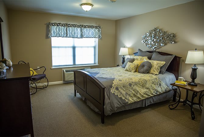 A cozy bedroom with a neatly made bed, decorative pillows, and a lamp by the window.