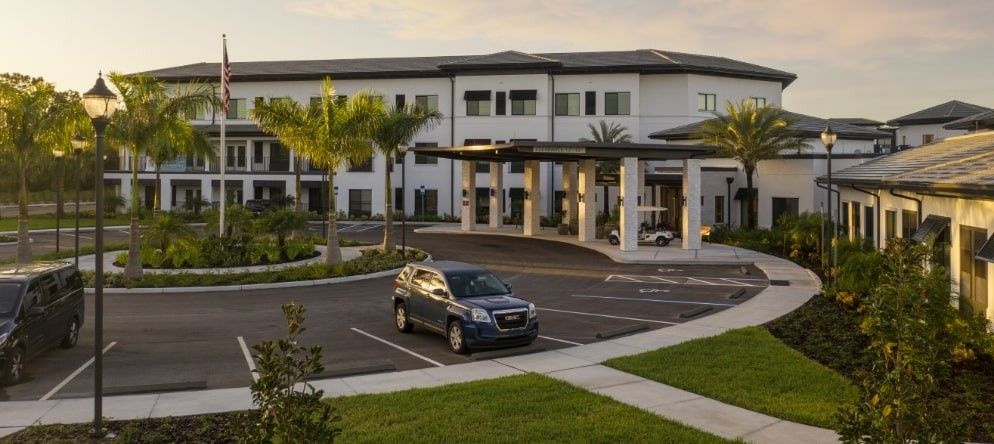 A modern building with a car parked in front, surrounded by palm trees under a clear sky.