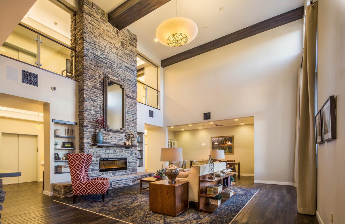 A spacious living room with a stone fireplace, modern furnishings, and a high ceiling.
