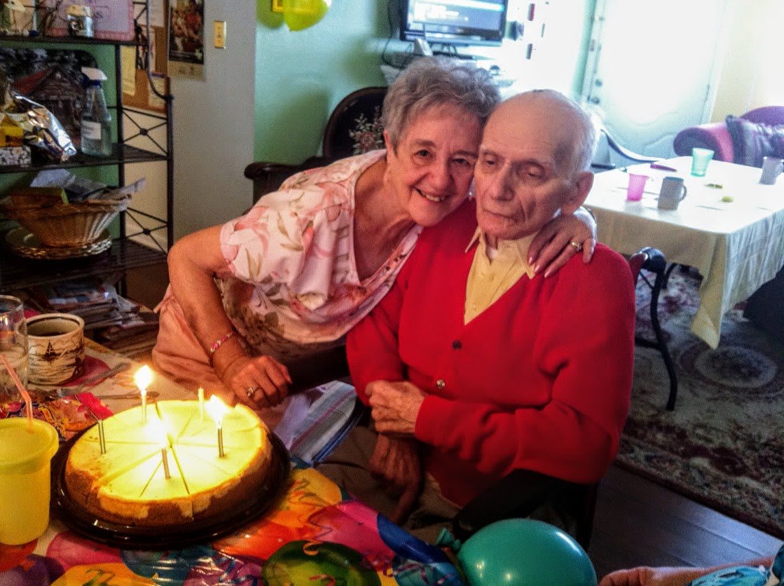 An elderly couple celebrating a birthday with a cake and lit candles.