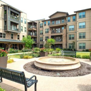 A modern apartment complex featuring a courtyard with a central fountain and surrounding benches.