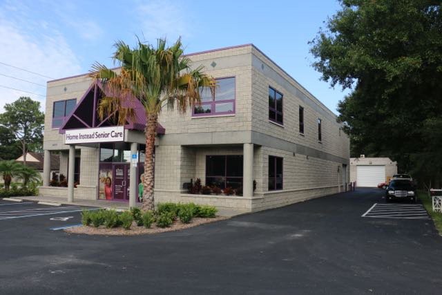 A commercial building with a palm tree in front and an adjacent parking area on a clear day.