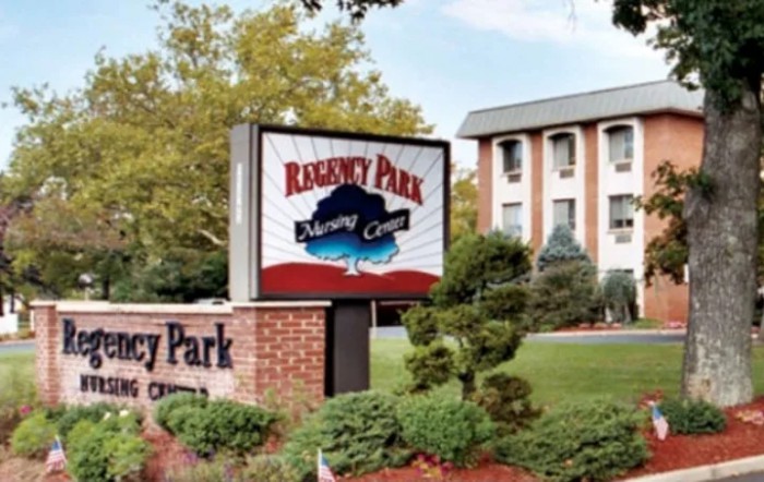 A nursing home's exterior sign with the building and landscaped grounds in the background.