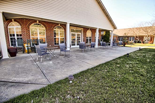 A patio area with chairs and tables outside a brick building with large windows.