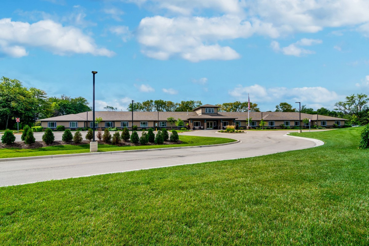 A large building surrounded by a grassy area with a winding road leading to it under a blue sky with clouds.
