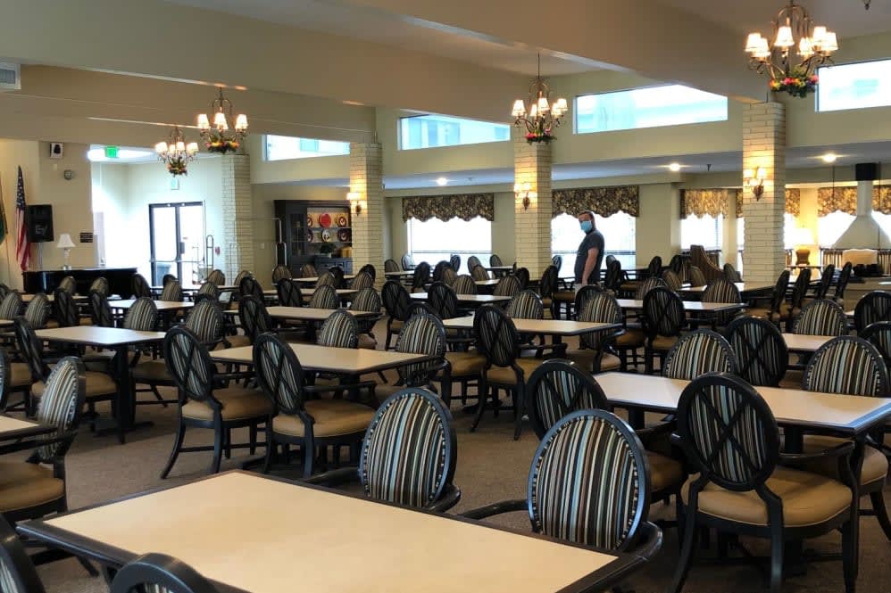 An empty dining room with rows of tables and chairs, illuminated by chandeliers.