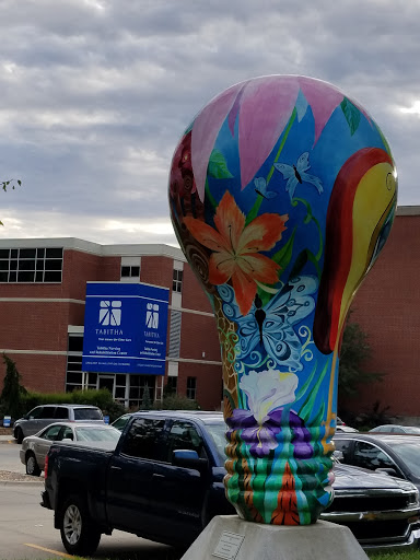 A vibrant, artistic light bulb sculpture stands out in front of a building.