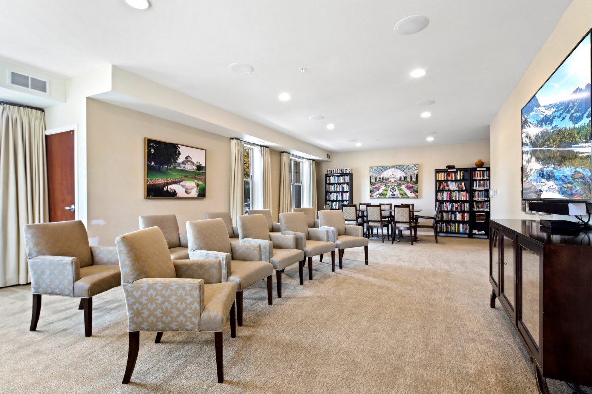 A spacious meeting room with rows of chairs, bookshelves, and paintings on the walls.