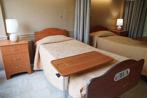 A view of a hospital room featuring two twin beds, a bedside table, and a privacy curtain.