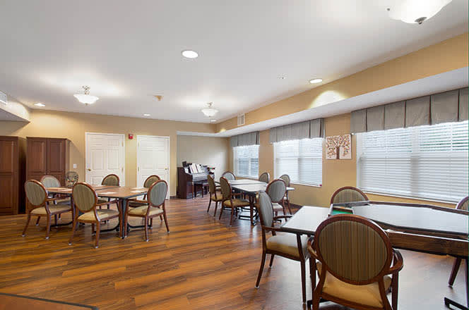 A spacious dining area with multiple tables and chairs set on a hardwood floor, featuring large windows and ceiling lights.