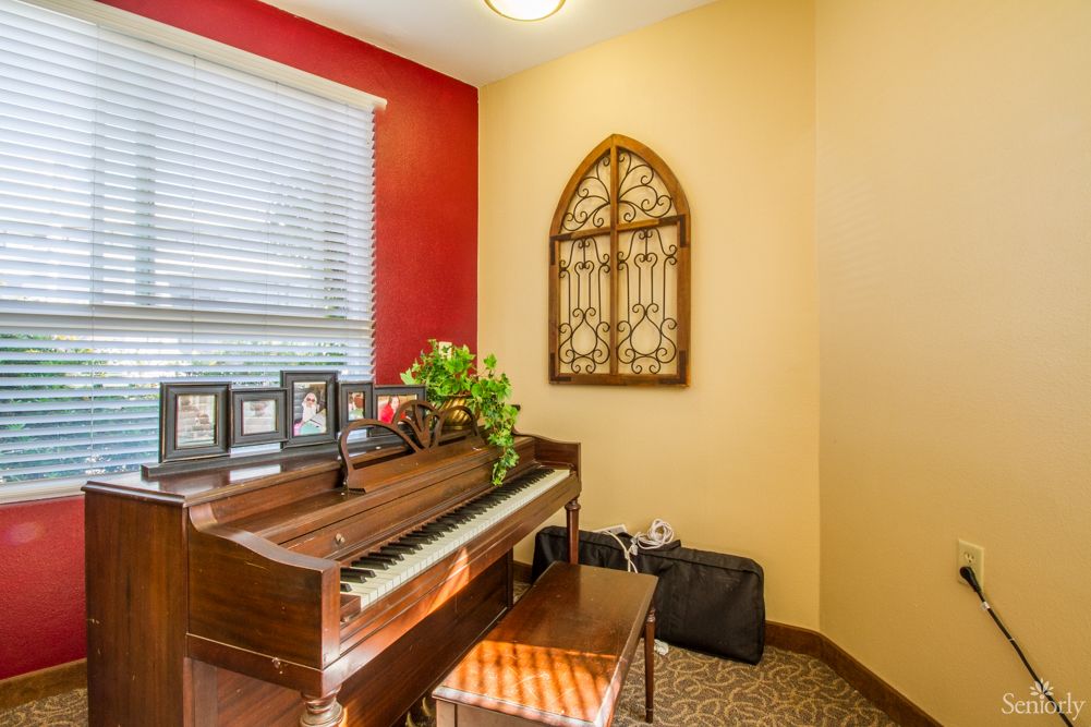 A cozy room featuring a piano, window with blinds, and decorative wall art.
