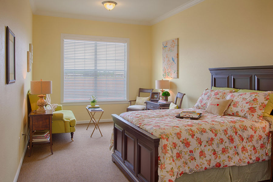A cozy bedroom with a floral bedspread, accented by warm lighting and seating area.