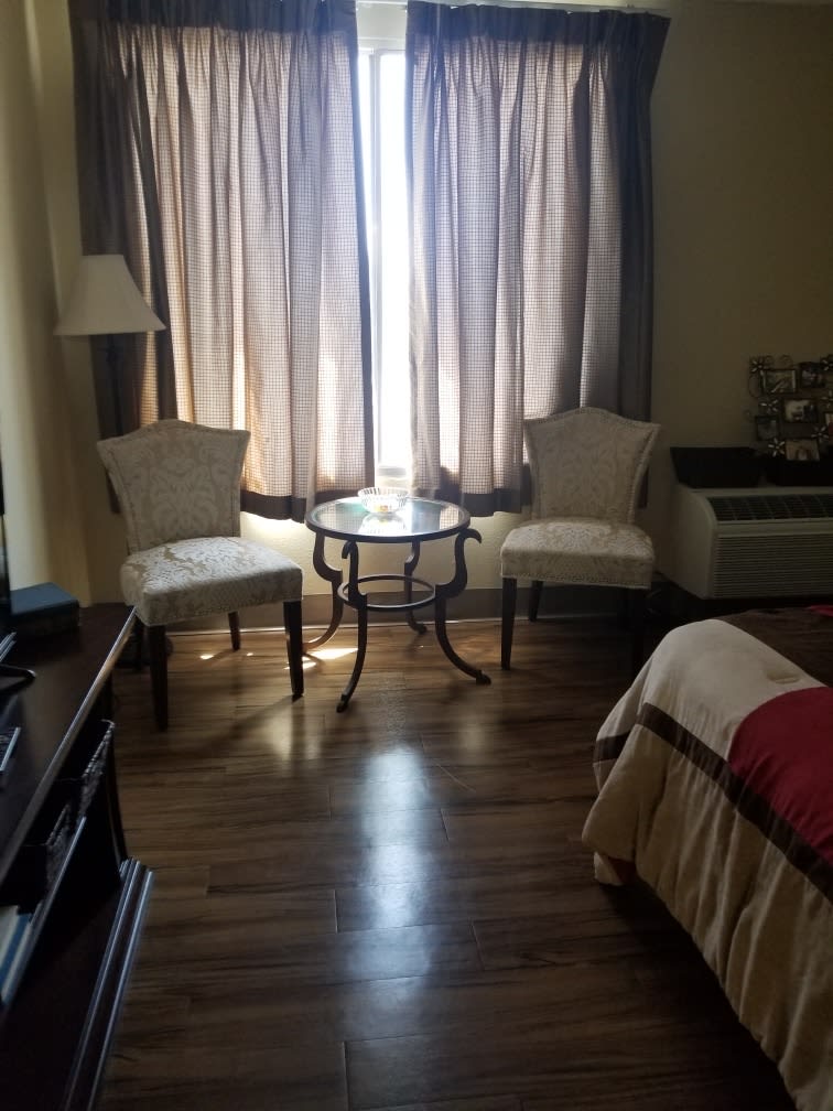 A well-lit hotel room featuring two chairs and a small table by the window.