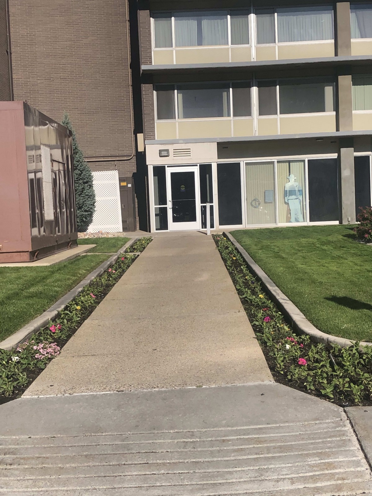 A pathway leads to the entrance of a building, with manicured grass and landscaping on either side.