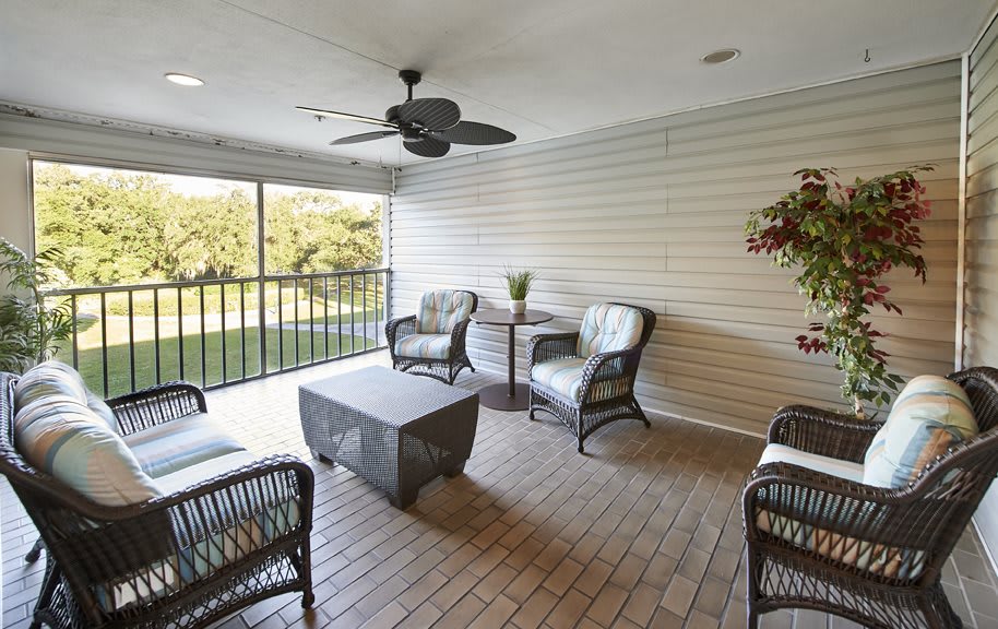 A cozy enclosed patio featuring wicker furniture, a ceiling fan, and natural light streaming in.