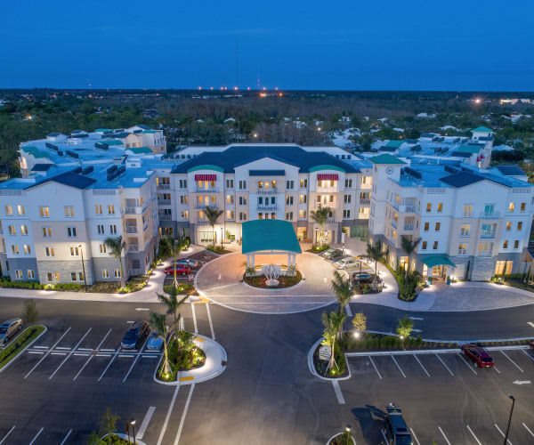 Aerial view of a well-lit hotel building with surrounding parking area at night.