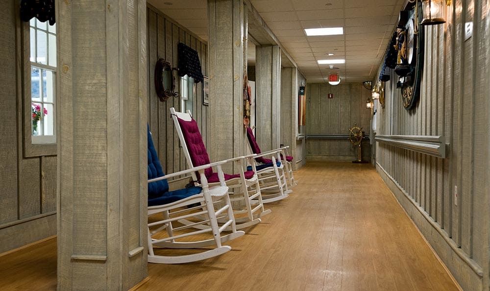 A quiet hallway with rocking chairs in a nursing home setting.