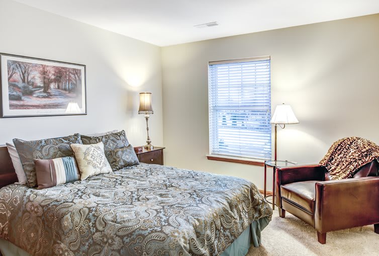 A cozy bedroom interior with a neatly made bed, lamps, and a window.