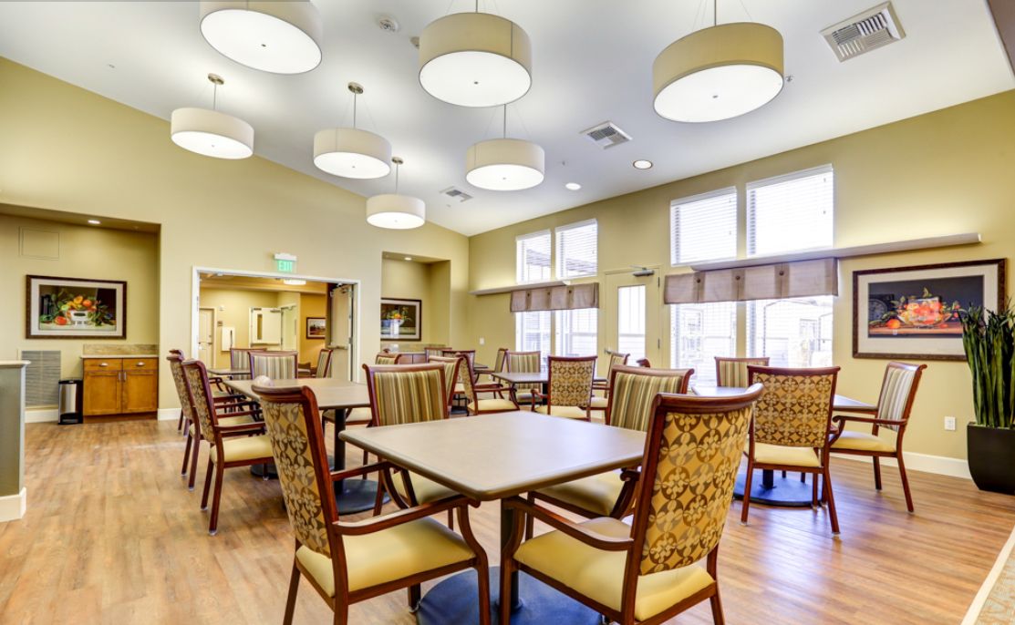 A modern dining room with elegant chairs and tables, featuring ample natural light from large windows.