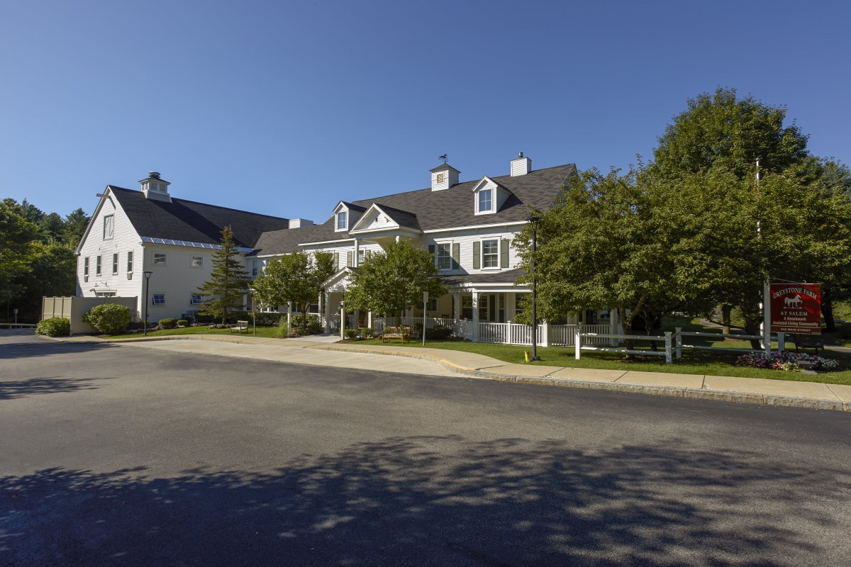 A picturesque view of a residential building with trees lining the road under a clear blue sky.