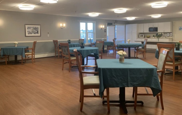 An empty dining room with neatly arranged tables and chairs, featuring wooden floors and soft lighting.