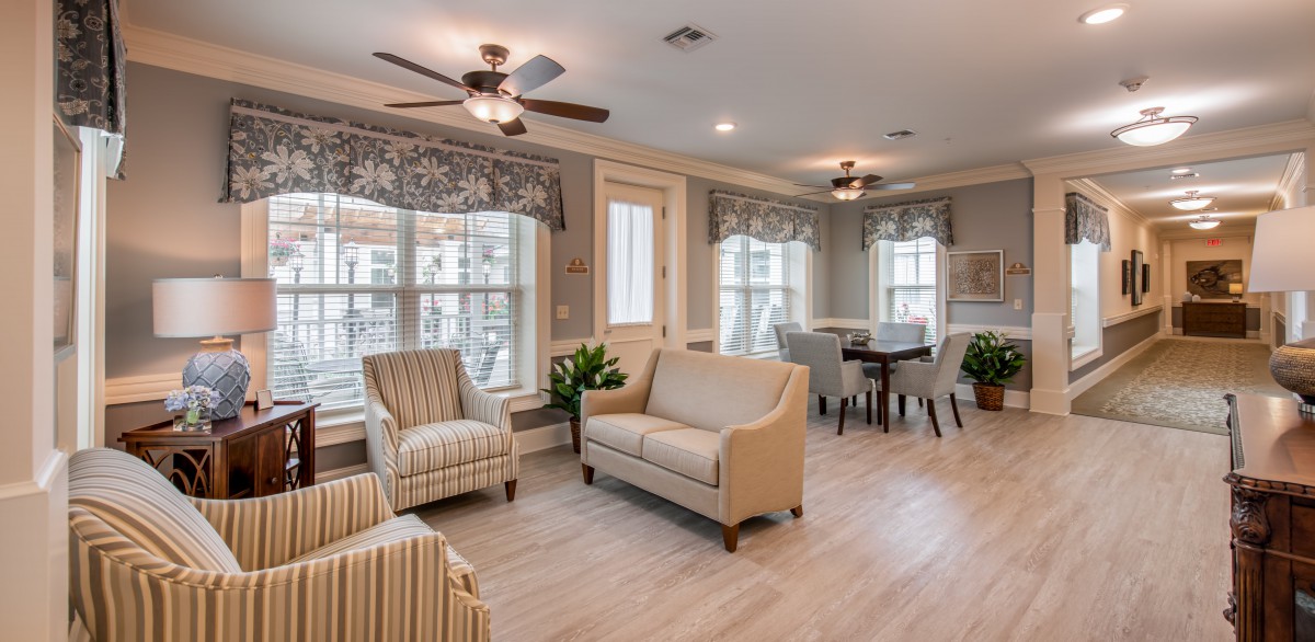 A cozy and well-lit living room with beige furniture, featuring a dining area and large windows.