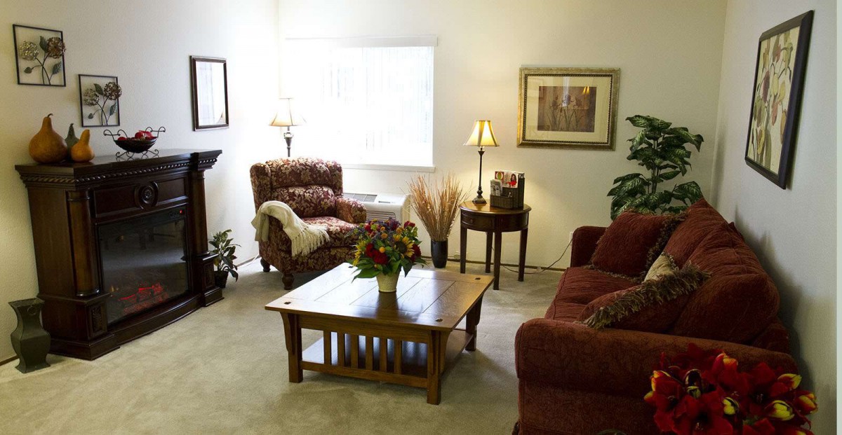 A cozy living room with a sofa, armchair, and coffee table, decorated with plants and artwork.