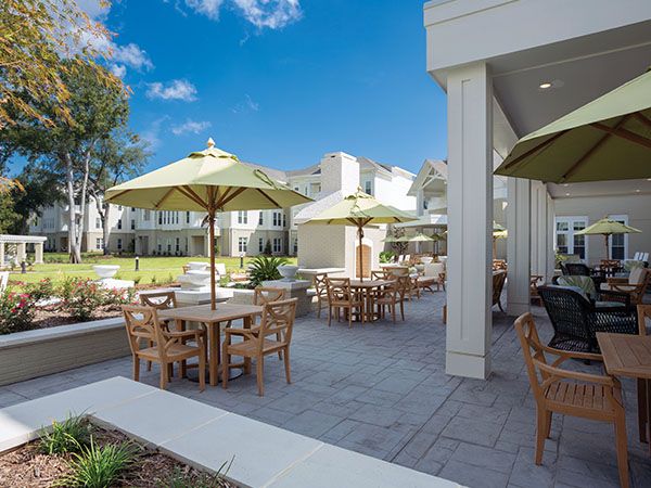 An outdoor patio area with tables, chairs, and umbrellas in front of a building on a sunny day.