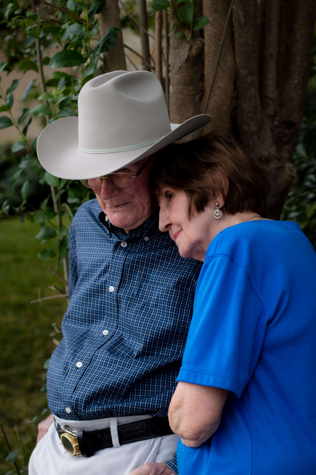 An elderly couple sharing a tender moment outdoors, with the man wearing a cowboy hat.