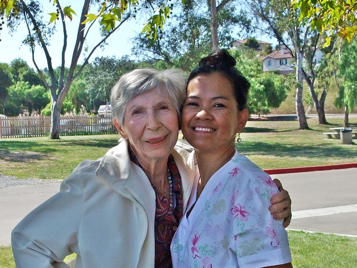 An elderly woman and a younger woman smiling together in a park.