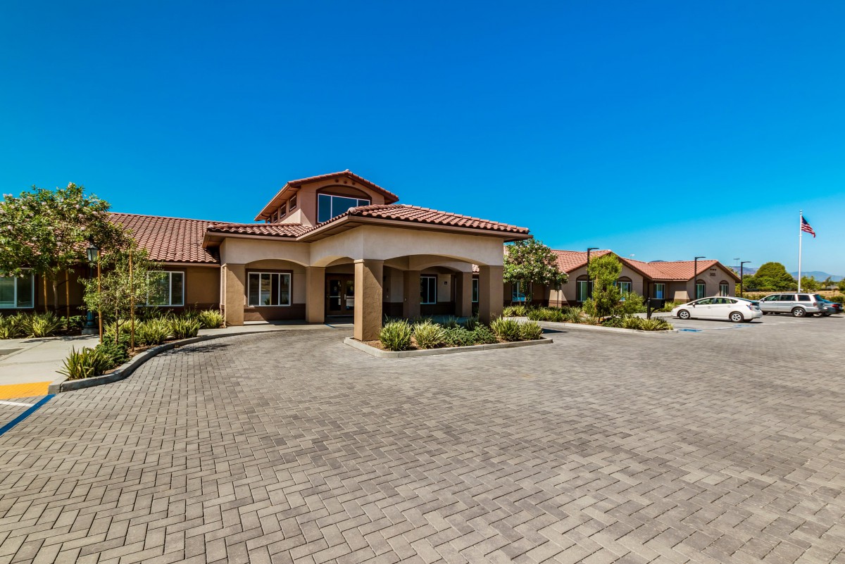 A residential building with a curved driveway and well-maintained landscaping under a clear blue sky.