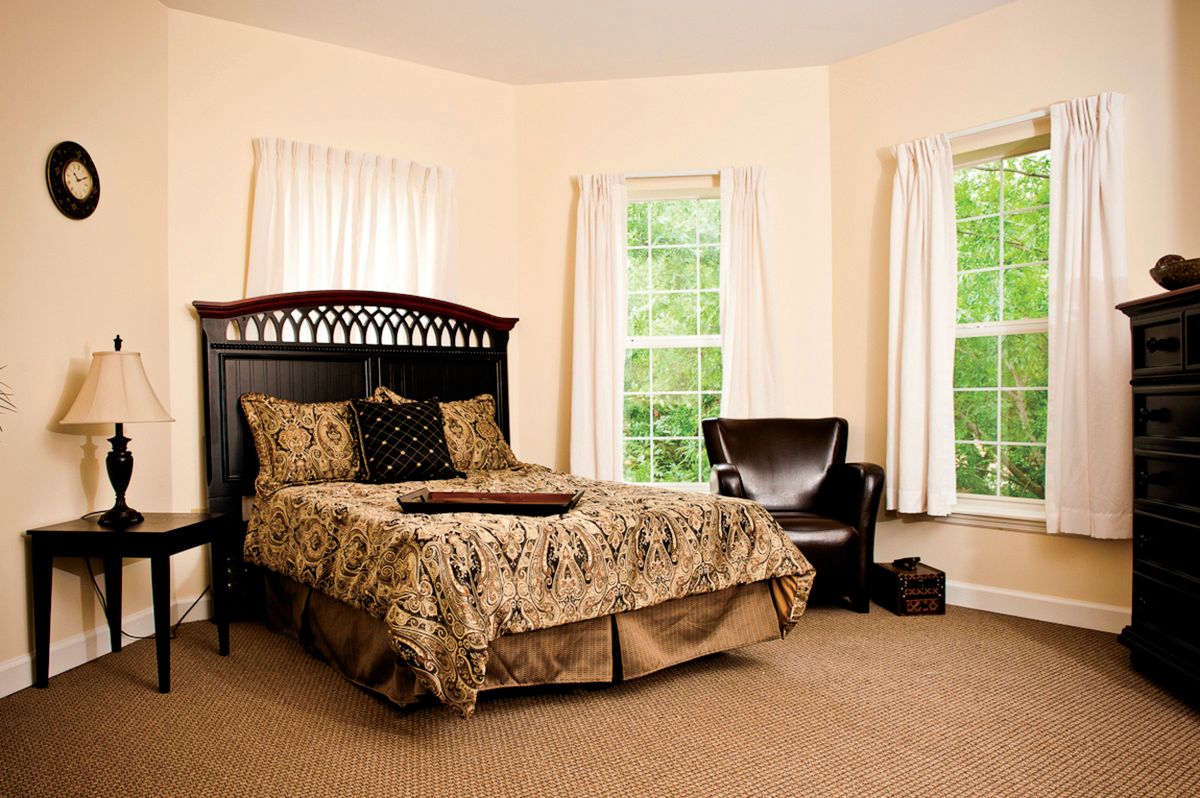 A cozy bedroom with a large bed, elegant bedding, and a comfortable chair by the windows.