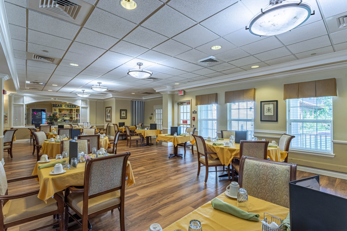 An elegant dining room with neatly arranged tables and chairs, featuring large windows and chandeliers.