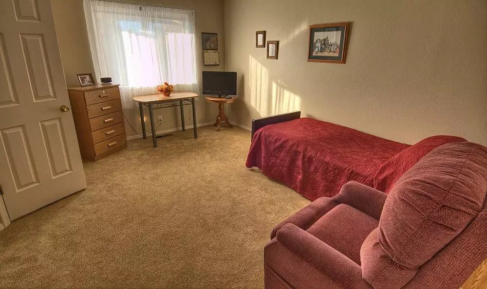 A cozy, carpeted bedroom with natural light and simple furniture.